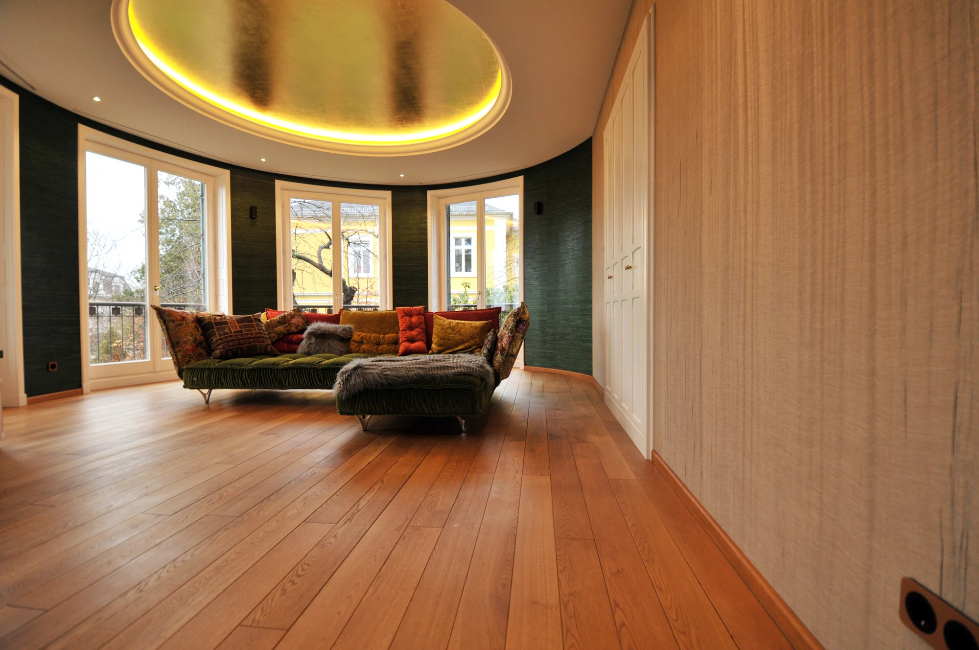 Wohnraum mit indirekt beleuchteter goldener Decke, grünem Sofa und abgestimmten Wandflächen